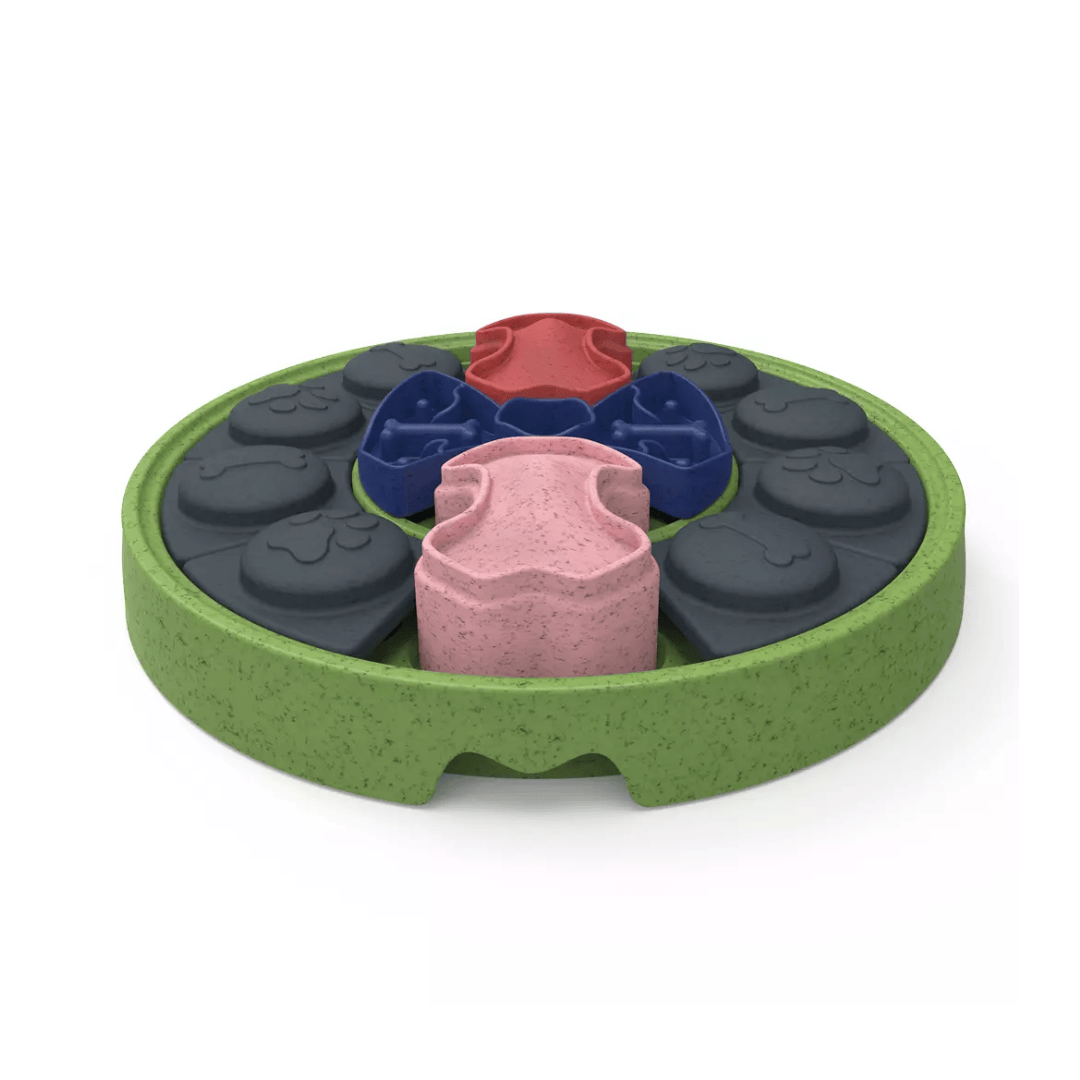 A circular green textured pet puzzle feeder with multiple compartments containing dark gray, blue, pink and red paw and bone embossed pieces shown on a white background.