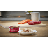The  Fish 4 Cats Tuna & Salmon cat food served on a plate with a soft, fish consistency. The tin is placed beside it. In the background there is fresh tuna and salmon on display.