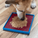 A dog licking a emat that is placed into the SodaPup Hold'em Suction Cup Holder. There is peanut butter spread over the lick mat.