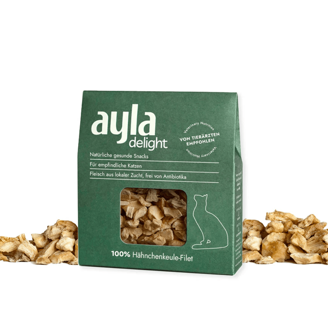 Green packaging of ayla delight cat snacks surrounded by chicken breasts on a white background