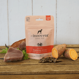 Bag of Innocent Hound Training Treats Tuna and Crab Rewards on a wooden surface, surrounded by raw ingredients and loose treats.