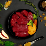 The fresh ingredients of the Canagan Venison and Wild Boar Stew Wet Food 400g in a bowl. There are other functional additions placed around the bowl including green lipped mussels.
